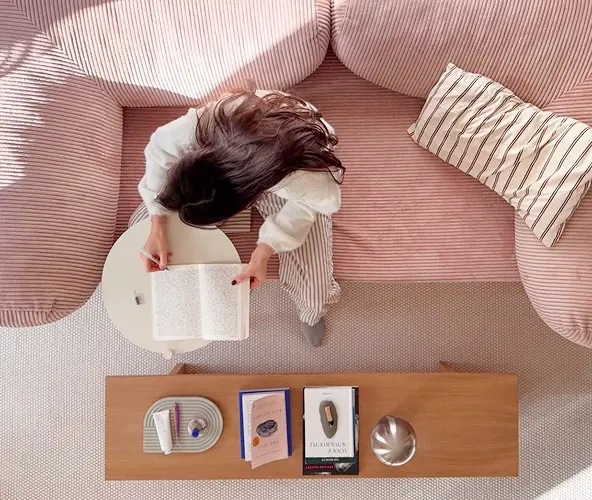 woman in her pajamas, on a pink couch, writing in her journal
